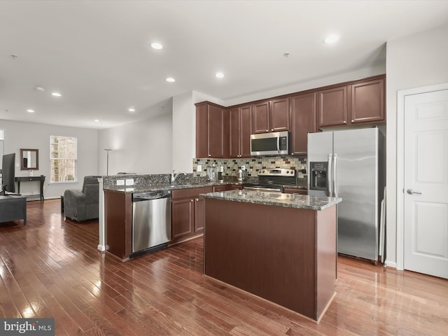 kitchen featuring stainless steel appliances, a center island, dark hardwood / wood-style flooring, decorative backsplash, and dark stone counters