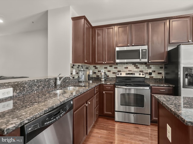 kitchen with tasteful backsplash, appliances with stainless steel finishes, sink, and dark stone countertops