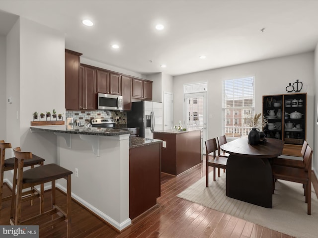 kitchen featuring dark stone countertops, backsplash, dark hardwood / wood-style floors, and appliances with stainless steel finishes