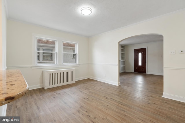 empty room featuring hardwood / wood-style flooring, a textured ceiling, radiator, and crown molding