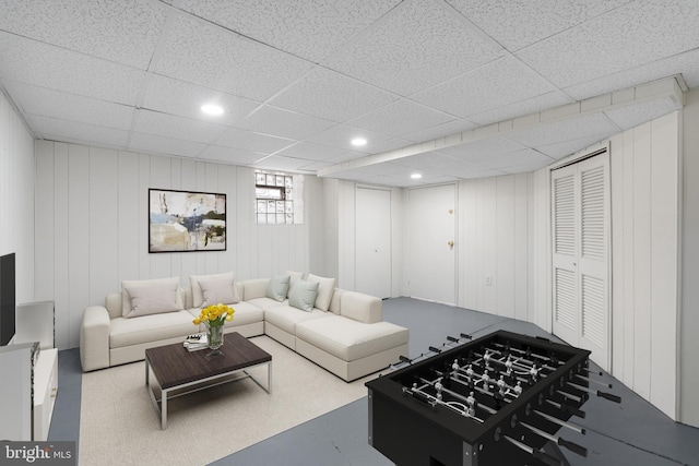 living room featuring a drop ceiling and wooden walls