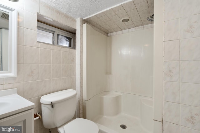 bathroom with toilet, vanity, tile walls, walk in shower, and a textured ceiling