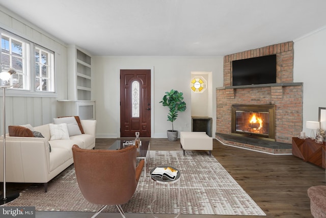 living room with dark wood-type flooring, built in shelves, a brick fireplace, and crown molding