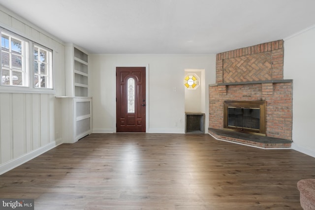 unfurnished living room featuring a brick fireplace, crown molding, dark hardwood / wood-style floors, and built in shelves