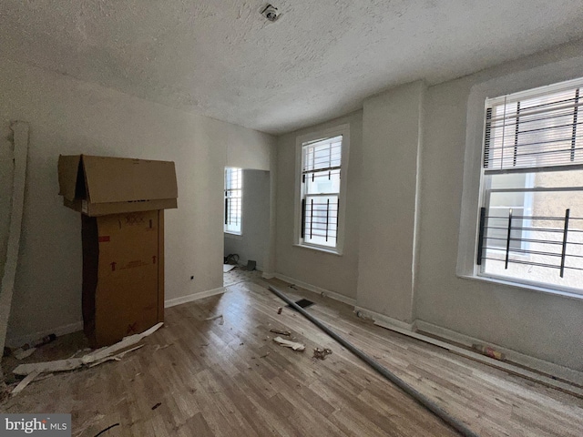 unfurnished living room with a textured ceiling, a wealth of natural light, and light hardwood / wood-style floors