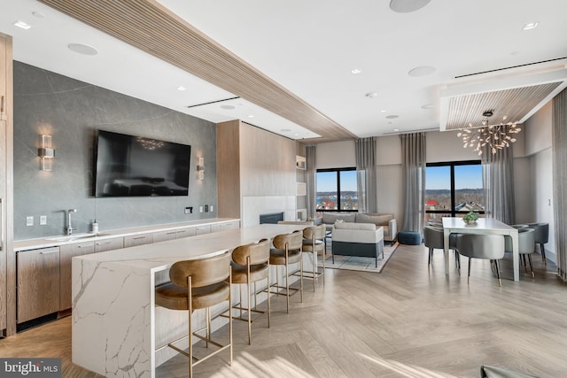 bar with light parquet floors, an inviting chandelier, a fireplace, light stone counters, and sink