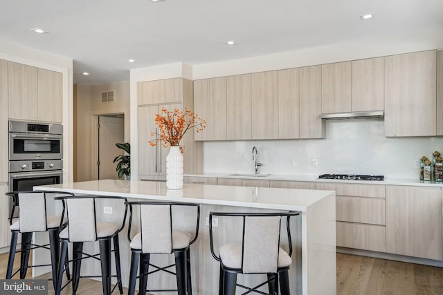 kitchen with a kitchen bar, sink, a center island, light brown cabinets, and light hardwood / wood-style floors