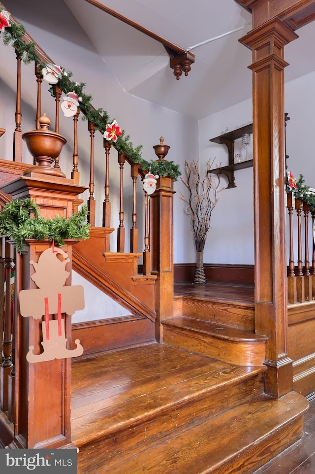 stairs with decorative columns and wood-type flooring