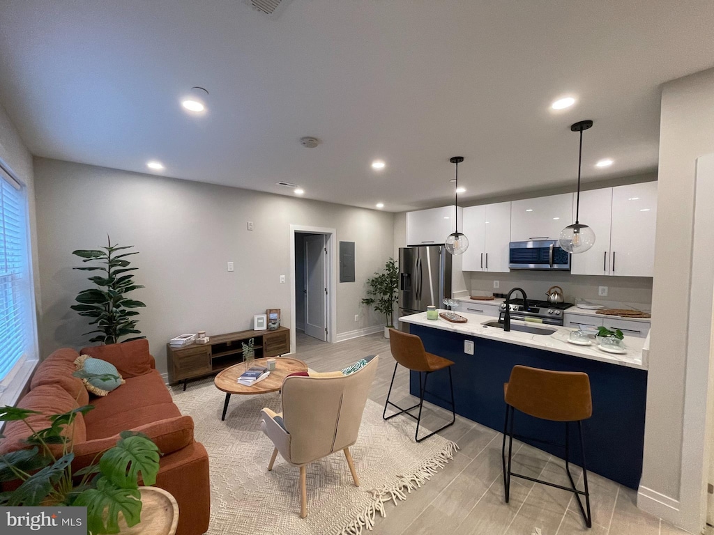 kitchen featuring pendant lighting, a kitchen bar, sink, white cabinetry, and stainless steel appliances