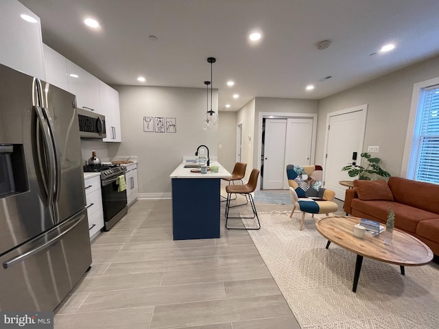 kitchen featuring appliances with stainless steel finishes, a kitchen island with sink, hanging light fixtures, white cabinets, and a breakfast bar