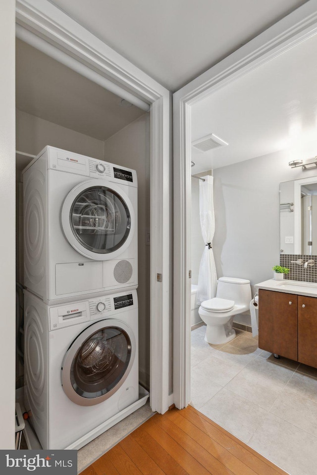 clothes washing area with sink, stacked washer and clothes dryer, and light hardwood / wood-style flooring