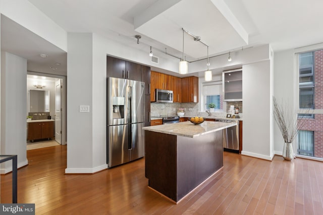 kitchen featuring appliances with stainless steel finishes, decorative backsplash, decorative light fixtures, light stone countertops, and a kitchen island