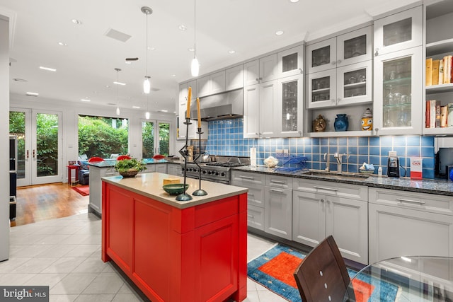 kitchen with light tile patterned floors, tasteful backsplash, a kitchen island, wall chimney exhaust hood, and sink