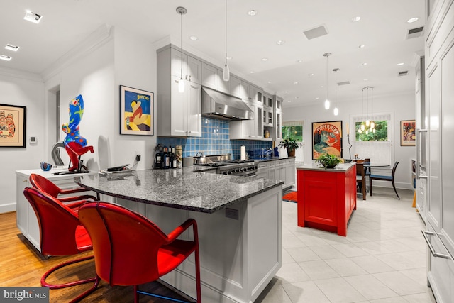 kitchen with dark stone countertops, a center island, hanging light fixtures, high end stainless steel range, and wall chimney exhaust hood