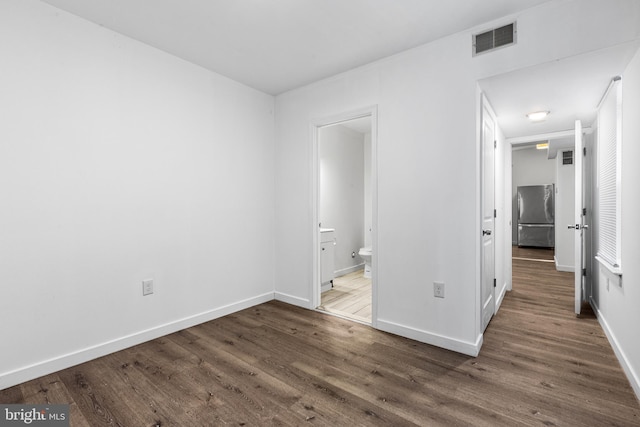 unfurnished bedroom featuring ensuite bathroom, dark hardwood / wood-style flooring, and stainless steel refrigerator