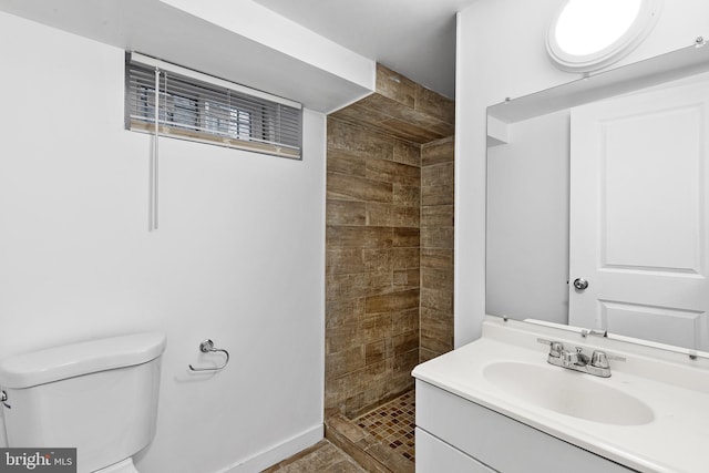 bathroom with toilet, a tile shower, and vanity