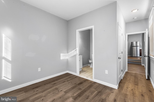 unfurnished bedroom featuring ensuite bathroom, hardwood / wood-style floors, and stainless steel refrigerator