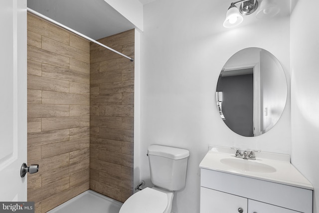 bathroom featuring toilet, a tile shower, and vanity