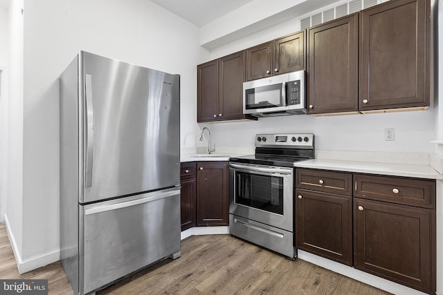 kitchen with appliances with stainless steel finishes, dark brown cabinets, and light hardwood / wood-style flooring