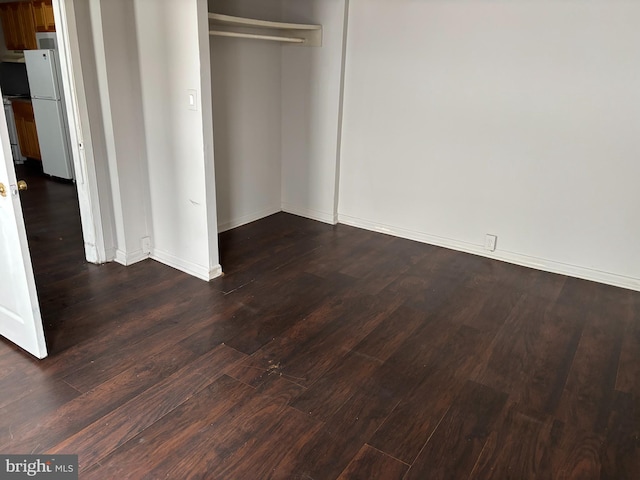 unfurnished bedroom featuring dark wood-type flooring, a closet, and white refrigerator