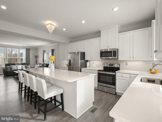 kitchen with appliances with stainless steel finishes, a kitchen island, white cabinetry, sink, and a kitchen breakfast bar