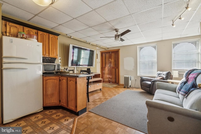 kitchen with ceiling fan, light parquet flooring, a drop ceiling, white fridge, and radiator heating unit