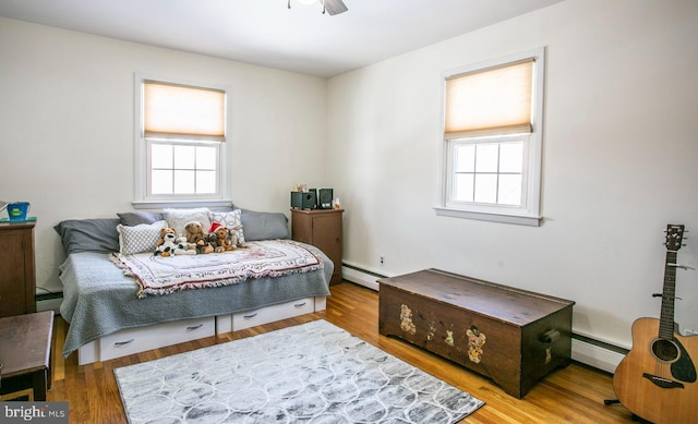 bedroom featuring multiple windows, ceiling fan, hardwood / wood-style flooring, and baseboard heating