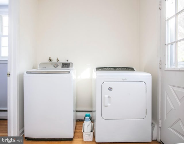 clothes washing area with a healthy amount of sunlight, a baseboard heating unit, washer and dryer, and light wood-type flooring