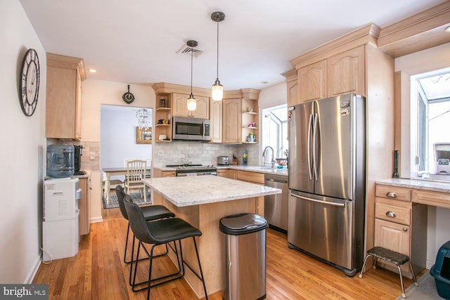 kitchen featuring light brown cabinetry, a center island, light hardwood / wood-style flooring, stainless steel appliances, and decorative backsplash