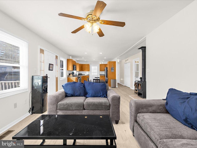 living room with light wood-type flooring, a wood stove, and ceiling fan