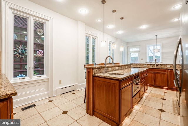 kitchen featuring sink, a center island with sink, baseboard heating, pendant lighting, and light stone countertops