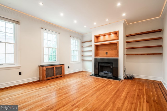 unfurnished living room featuring built in shelves, ornamental molding, and light hardwood / wood-style floors