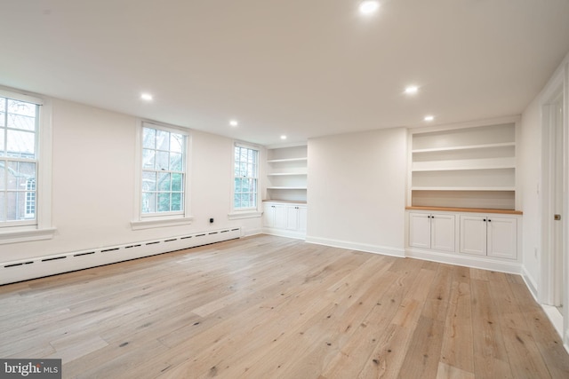 unfurnished living room with baseboard heating, built in shelves, and light hardwood / wood-style flooring