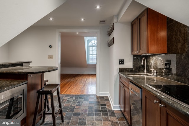 kitchen with dark stone countertops, a breakfast bar area, sink, and stainless steel dishwasher