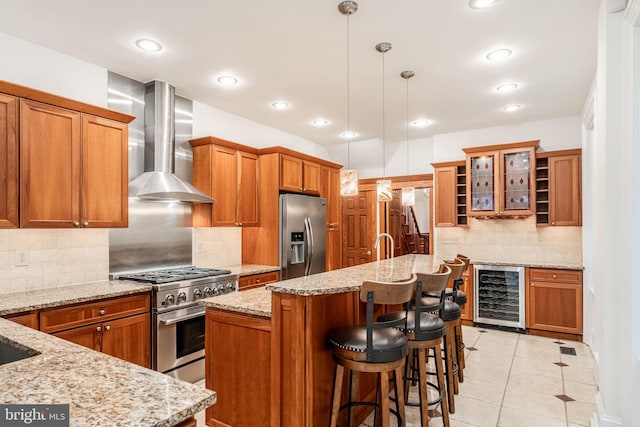 kitchen featuring decorative light fixtures, an island with sink, stainless steel appliances, beverage cooler, and wall chimney range hood