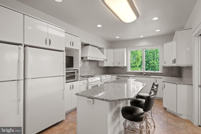 kitchen with a kitchen island, white cabinetry, appliances with stainless steel finishes, custom range hood, and light stone counters