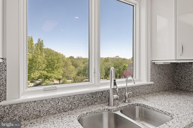 room details with backsplash, light stone countertops, sink, and white cabinetry