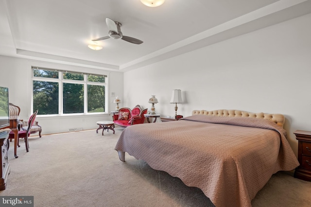 carpeted bedroom with ceiling fan and a raised ceiling