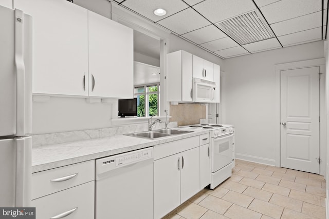 kitchen with white appliances, white cabinets, a paneled ceiling, sink, and light tile patterned floors