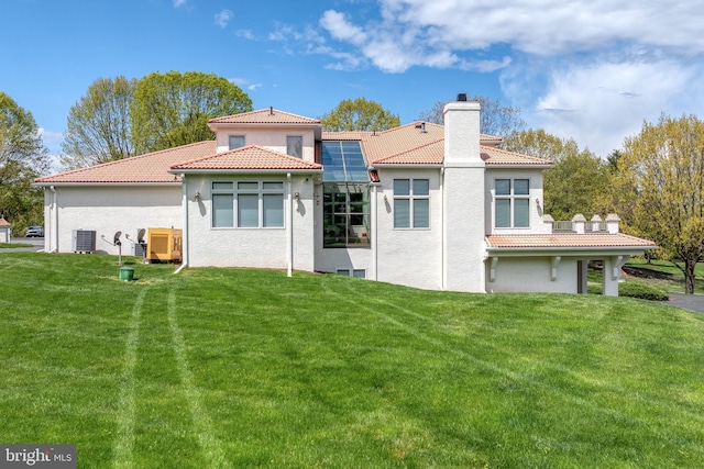 back of property with cooling unit, a yard, and solar panels