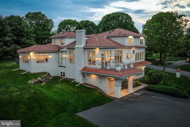 back house at dusk with a balcony and a yard