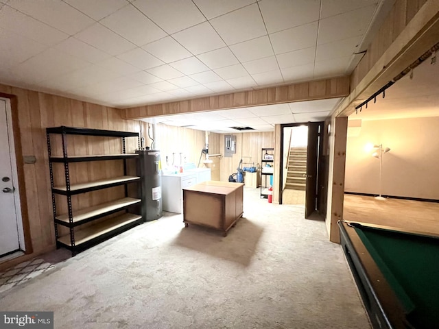 basement featuring wood walls, carpet flooring, electric panel, electric water heater, and washer and clothes dryer