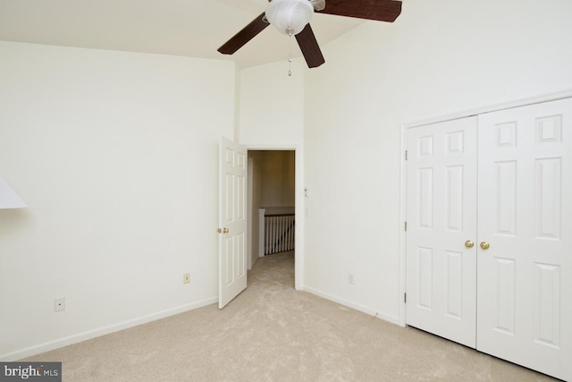 unfurnished bedroom with a ceiling fan, baseboards, high vaulted ceiling, a closet, and light carpet