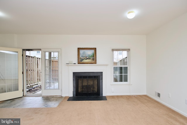 unfurnished living room with carpet flooring, visible vents, baseboards, and a fireplace with flush hearth