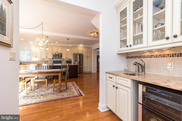 kitchen featuring light stone countertops, pendant lighting, appliances with stainless steel finishes, sink, and light wood-type flooring