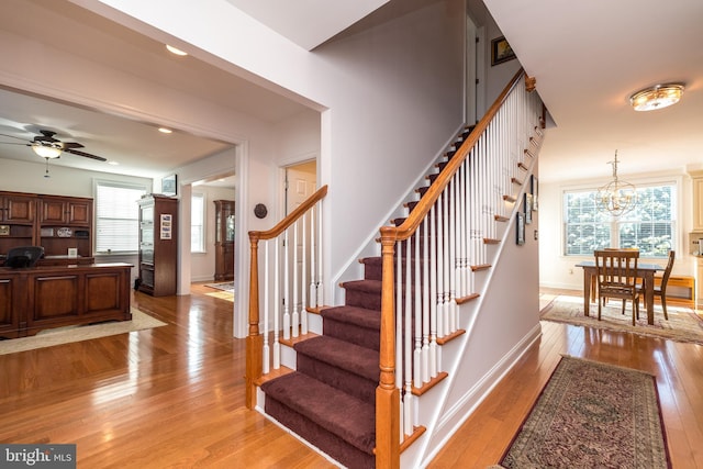 staircase with ceiling fan with notable chandelier and hardwood / wood-style floors