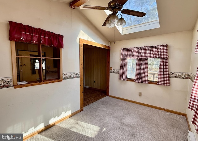 unfurnished room featuring ceiling fan, vaulted ceiling with skylight, and carpet flooring