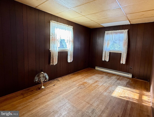 empty room with a baseboard radiator, a drop ceiling, and wooden walls