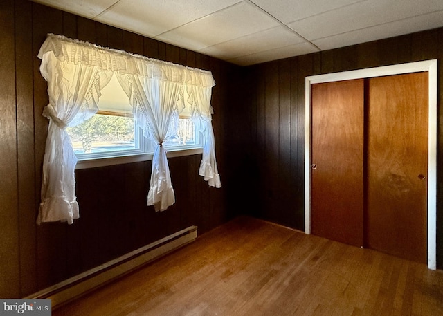 unfurnished bedroom featuring a closet, hardwood / wood-style floors, baseboard heating, and wood walls