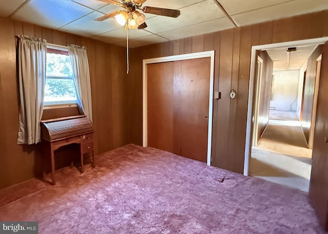 unfurnished bedroom with ceiling fan, carpet, a closet, and wood walls